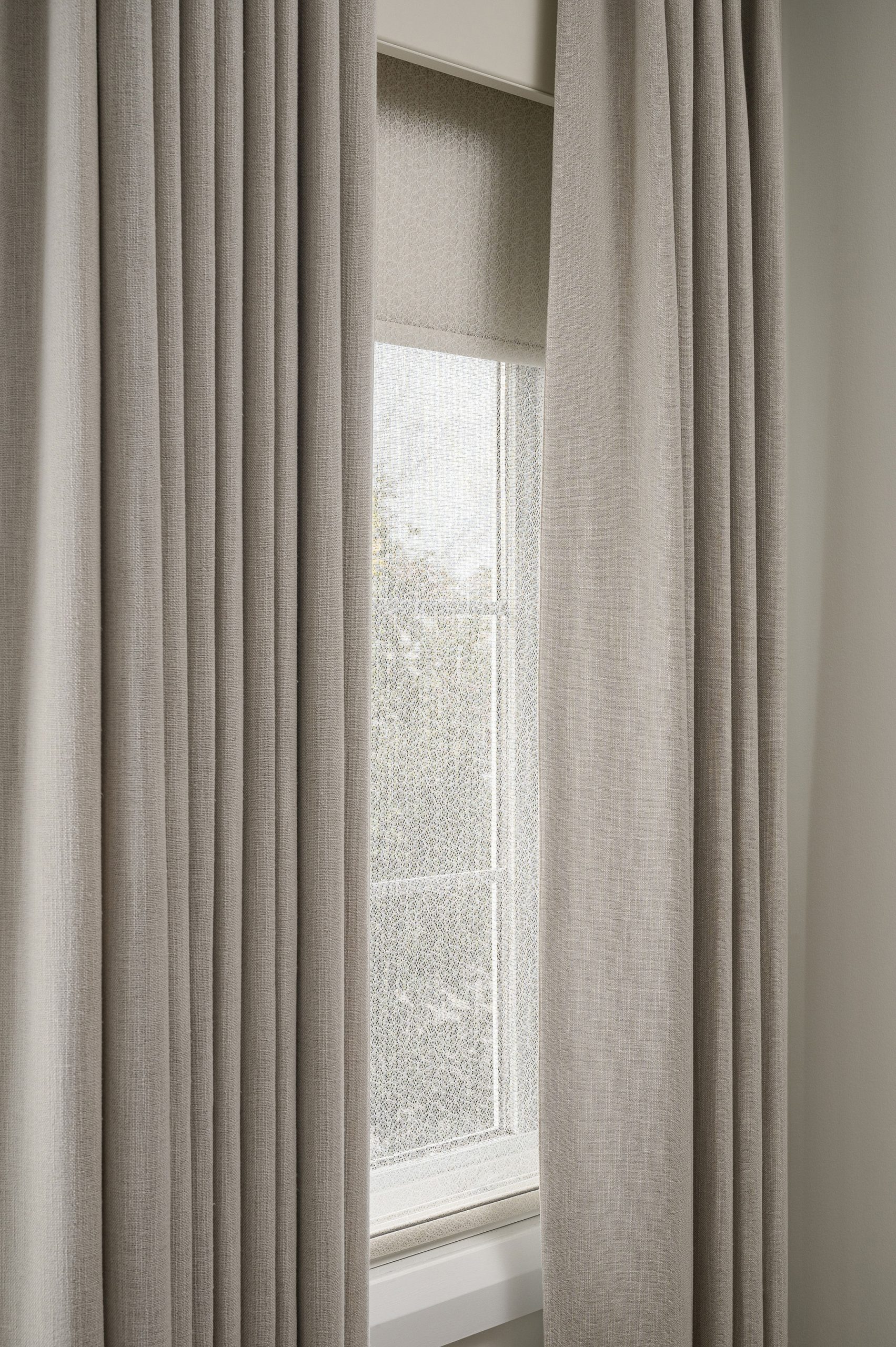 Layered window treatment with warm greige linen drapes over a textured sheer roller shade