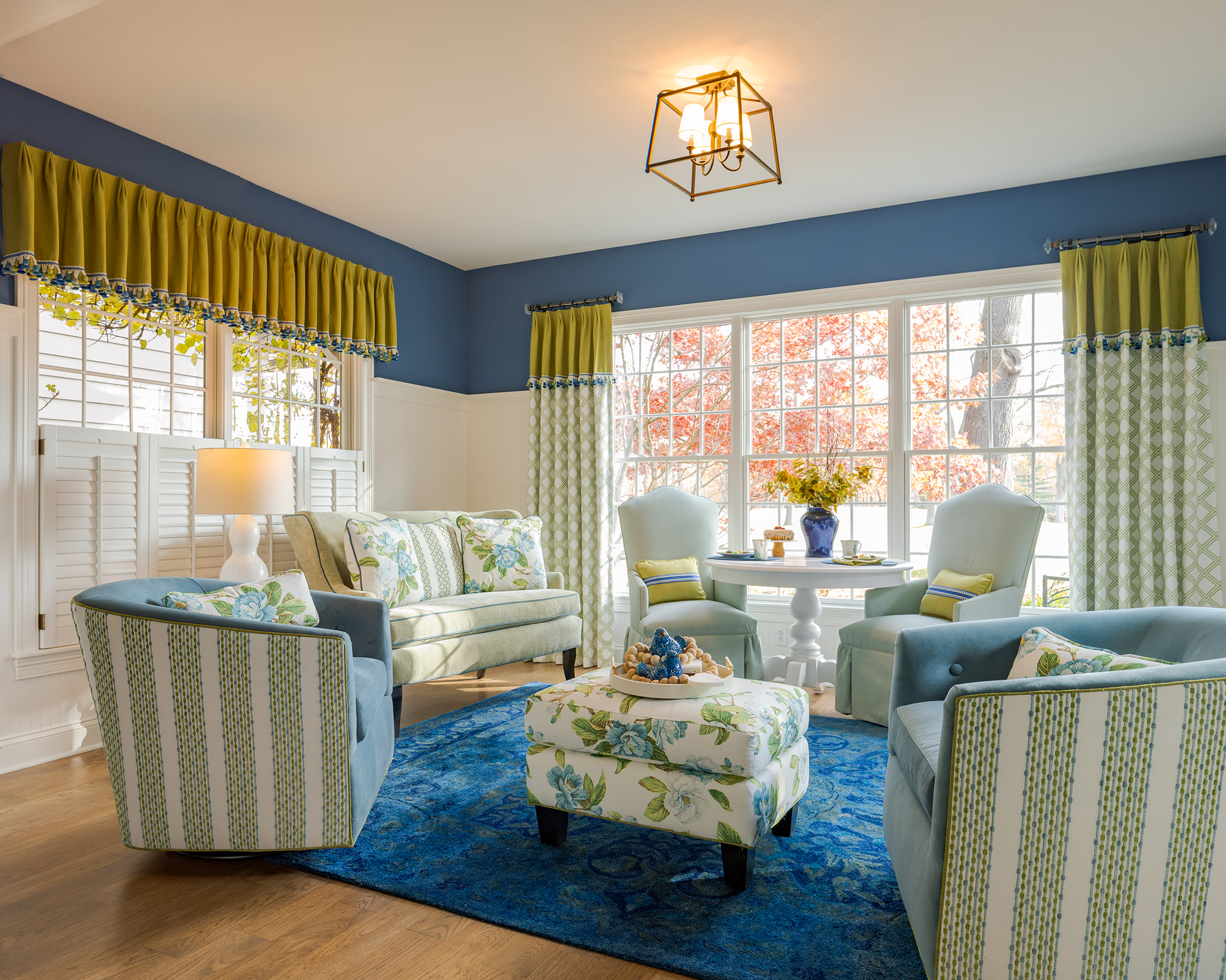 Colorful Connecticut living room with layered patterns in blue and green, featuring bold window treatments and floral ottoman