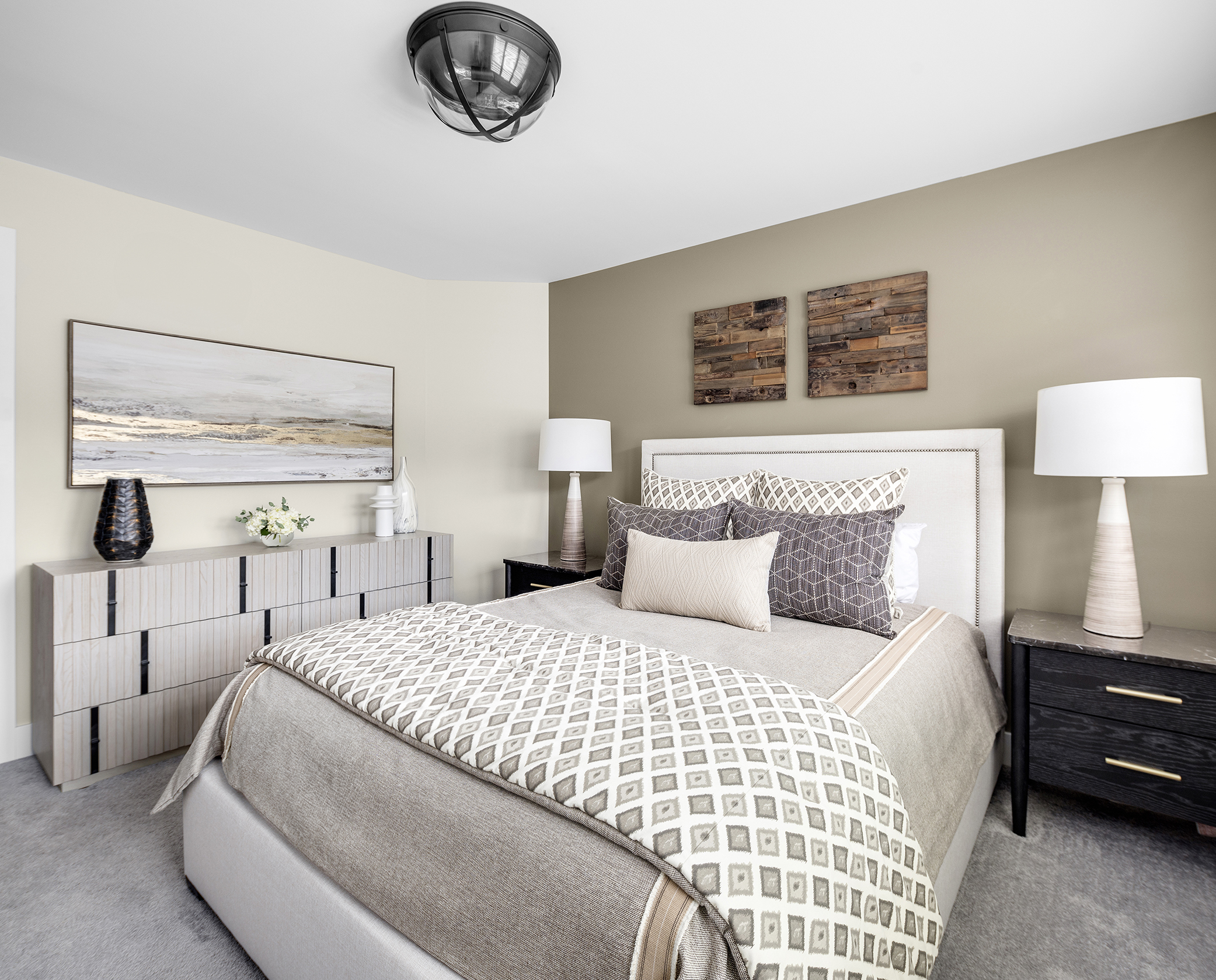 Transitional bedroom with olive accent wall, neutral bedding with geometric patterns and rustic wood art