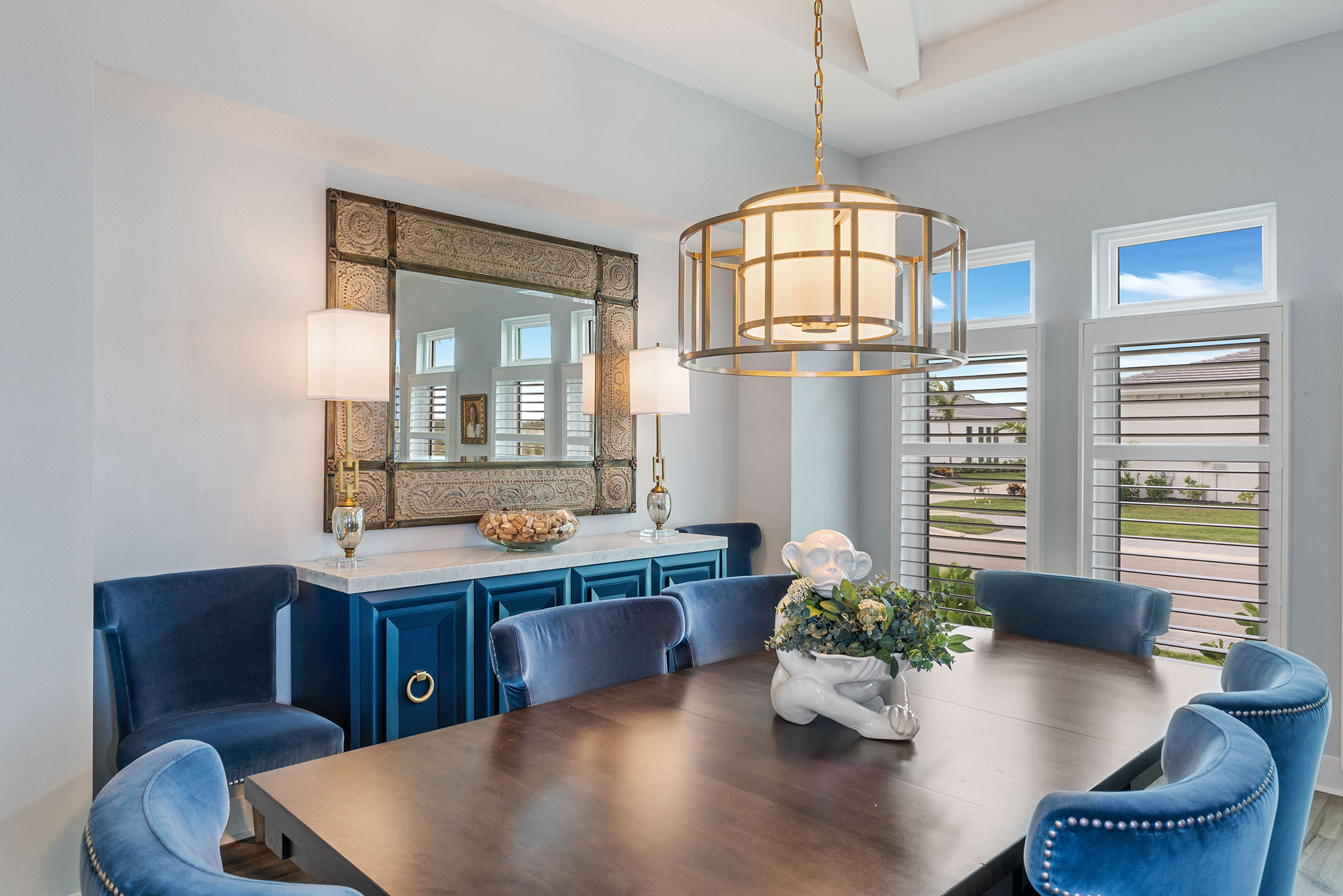 Bold dining room with blue velvet chairs, teal buffet, and gold drum pendant chandelier